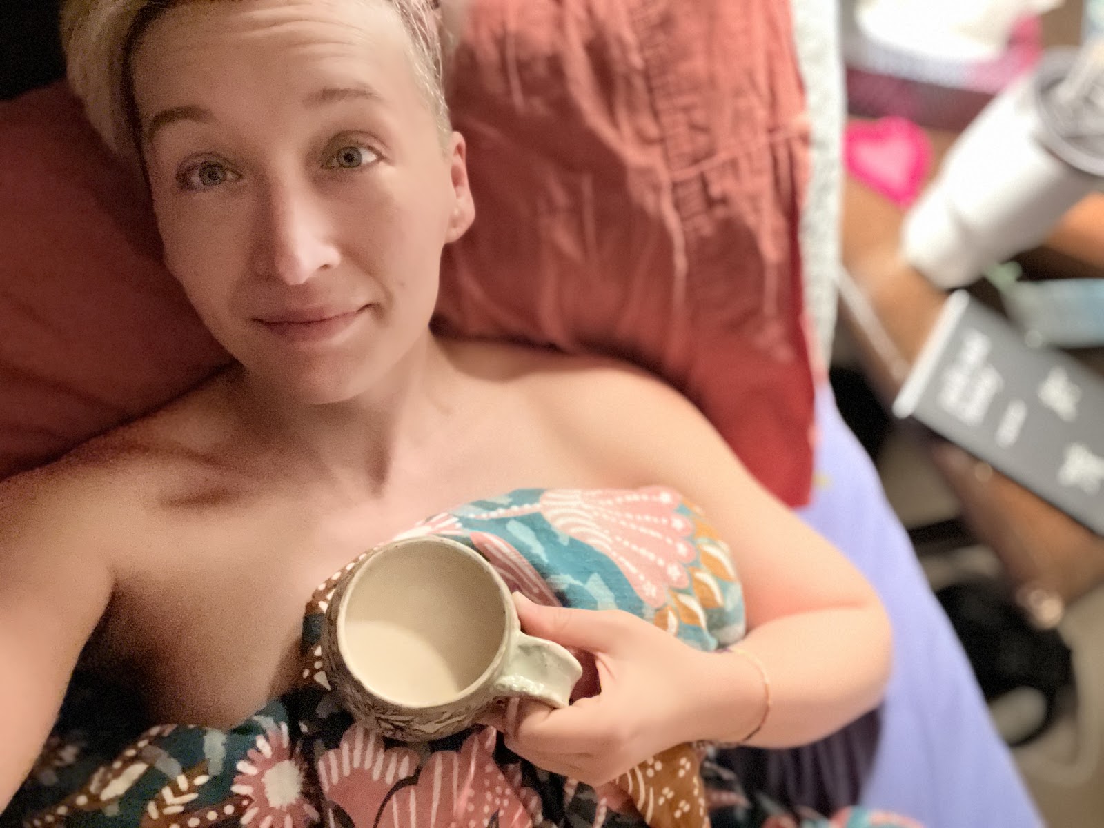 Tarzan lies naked in bed with a coffee cup in hand, her head resting on a peach pilllow case, covered to the shoulders colourful plant-themed anthropologie duvet cover (no nudity in this one - your screen reader isn't holding back, promise)