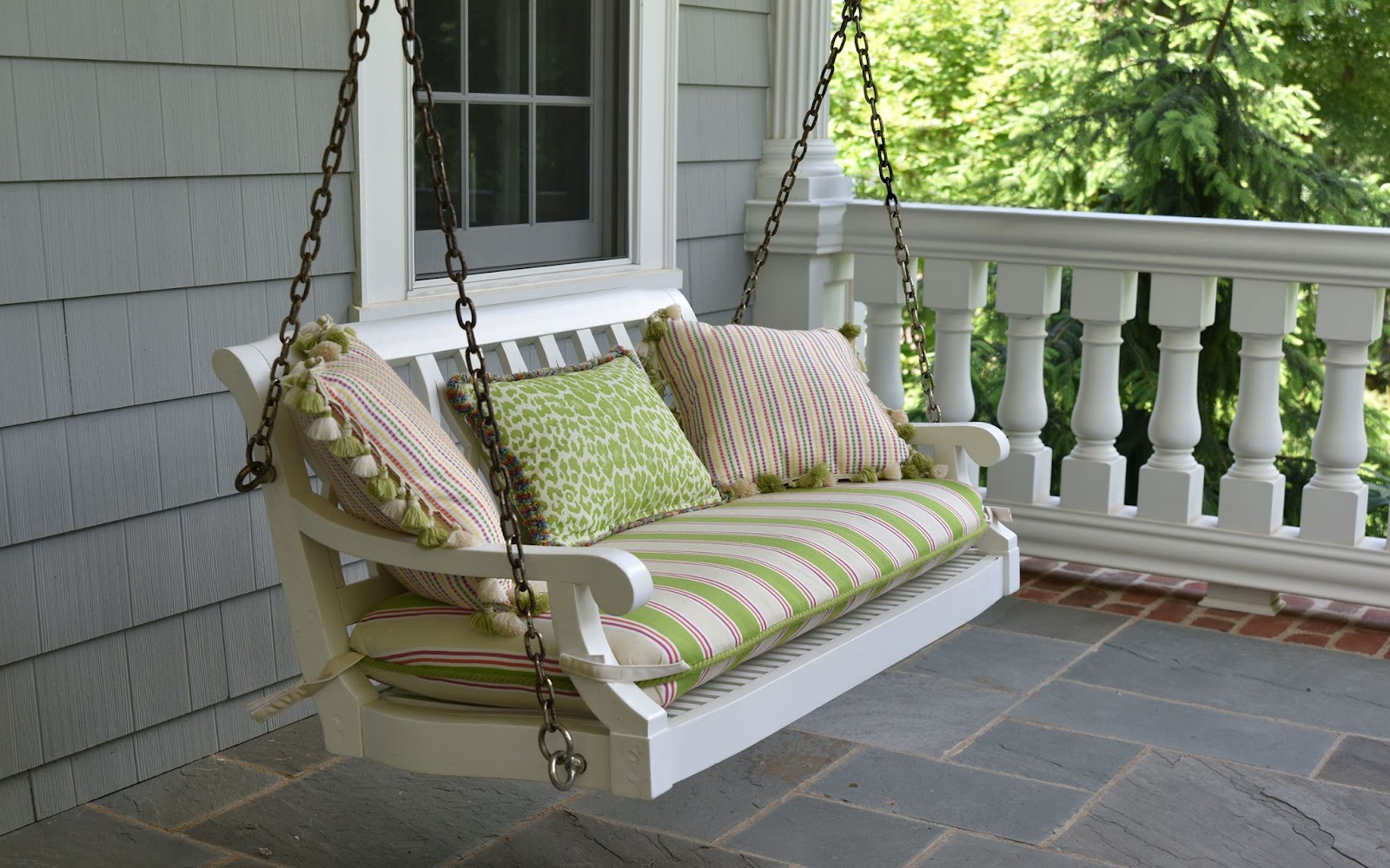 white wooden porch swing with green striped cushions and several plush pillows