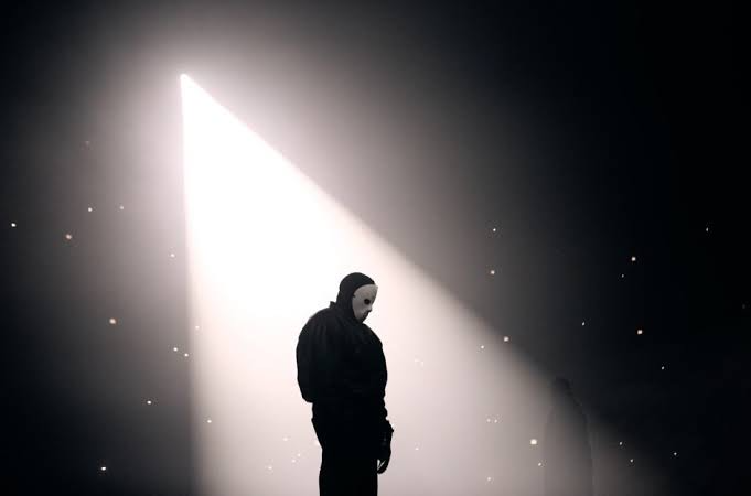 A person in a mask standing in a dark room

Description automatically generated