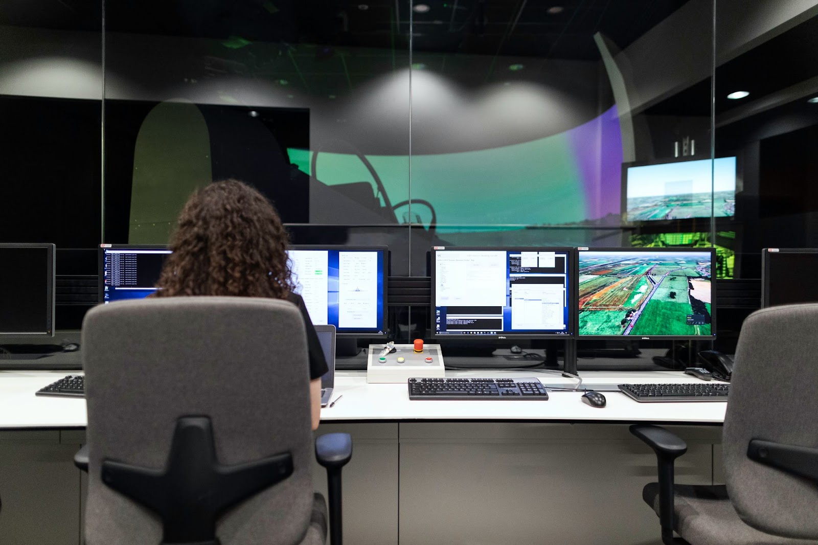 A person in an operations center surrounded by screens displaying various data visualizations and code.