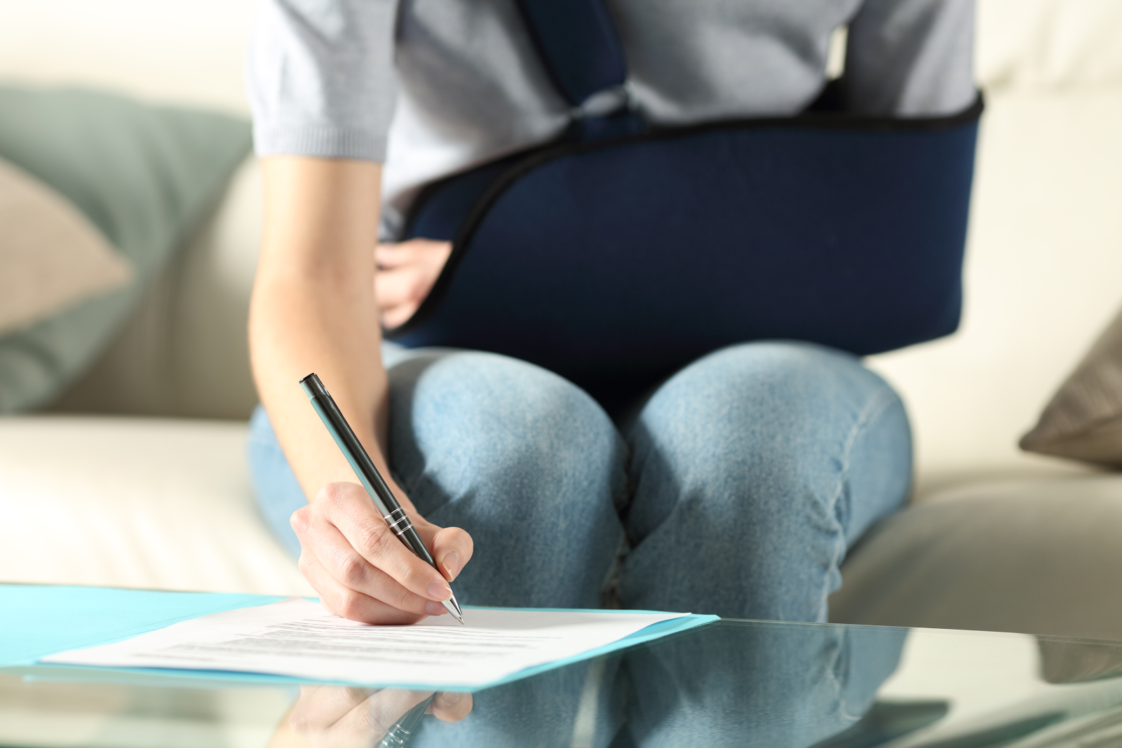 photo of a woman in an arm sling filing out a piece of paper from her own insurance provider on a coffee table, personal injury lawsuit theme