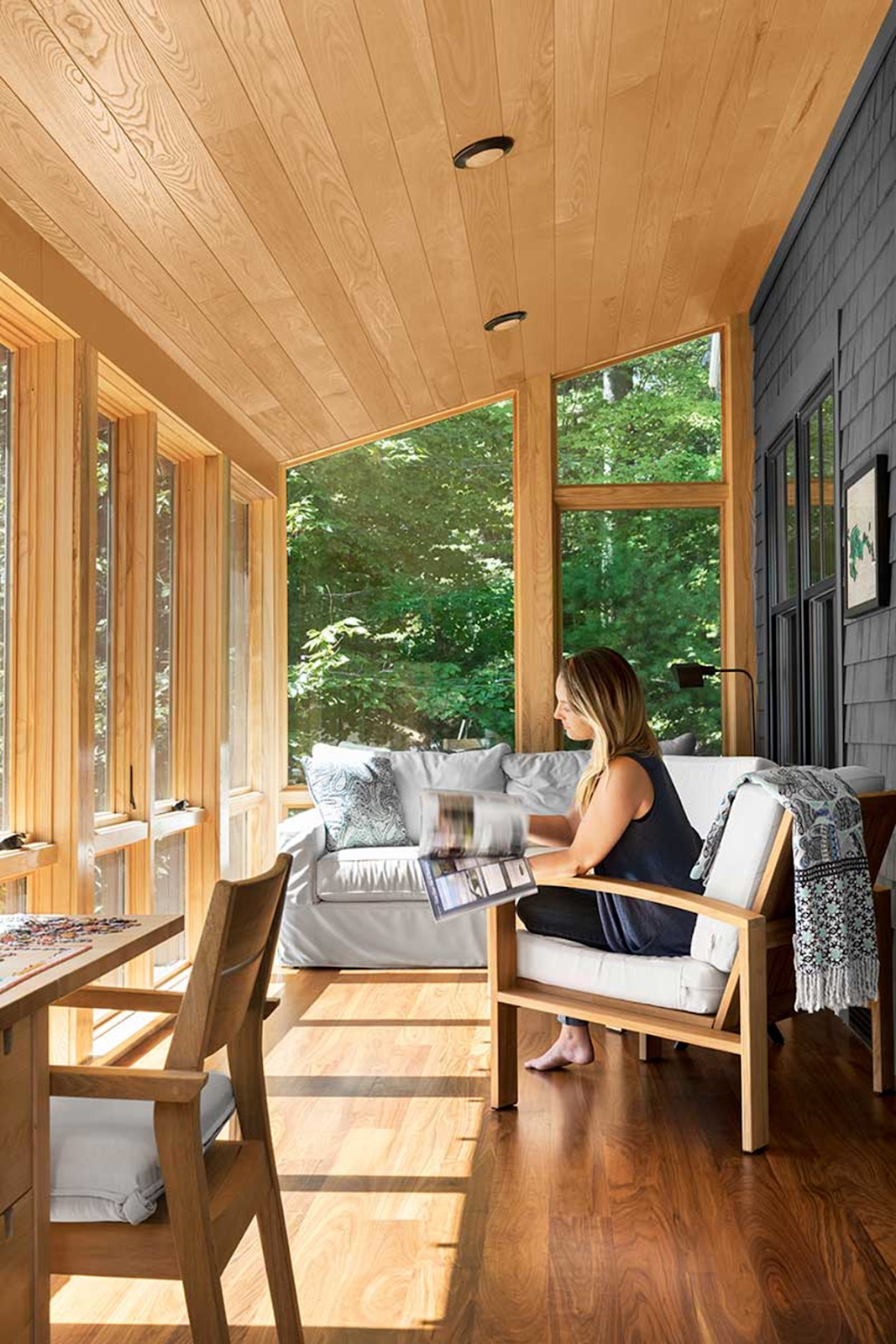 The picture depicts a person sitting on a chair, flipping through a magazine. There are numerous windows in this space, letting in beautiful, natural light.