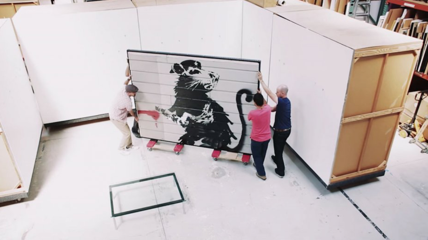 3 people transporting a large banksy mural that has been cut out of a building. It is going into secured storage at FACL.