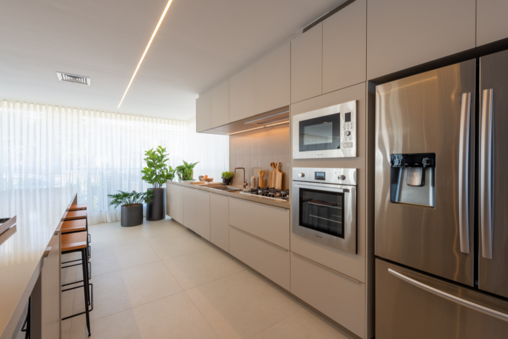 Cozinha planejada com módulos brancos, eletrodomésticos inox e janela com plantas ao fundo.