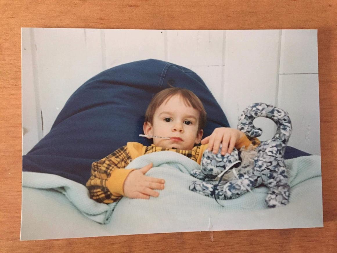 Baby Stephan lies in bed, holding a stuffed animal.