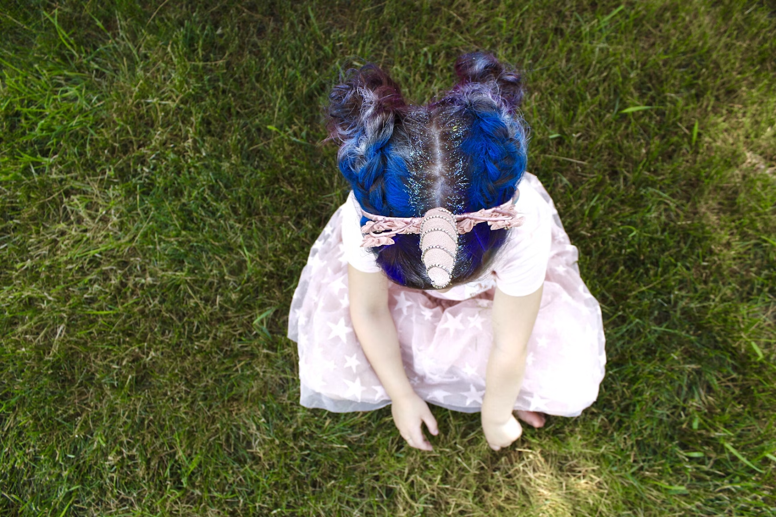 a little girl in a unicorn costume sits on grass
