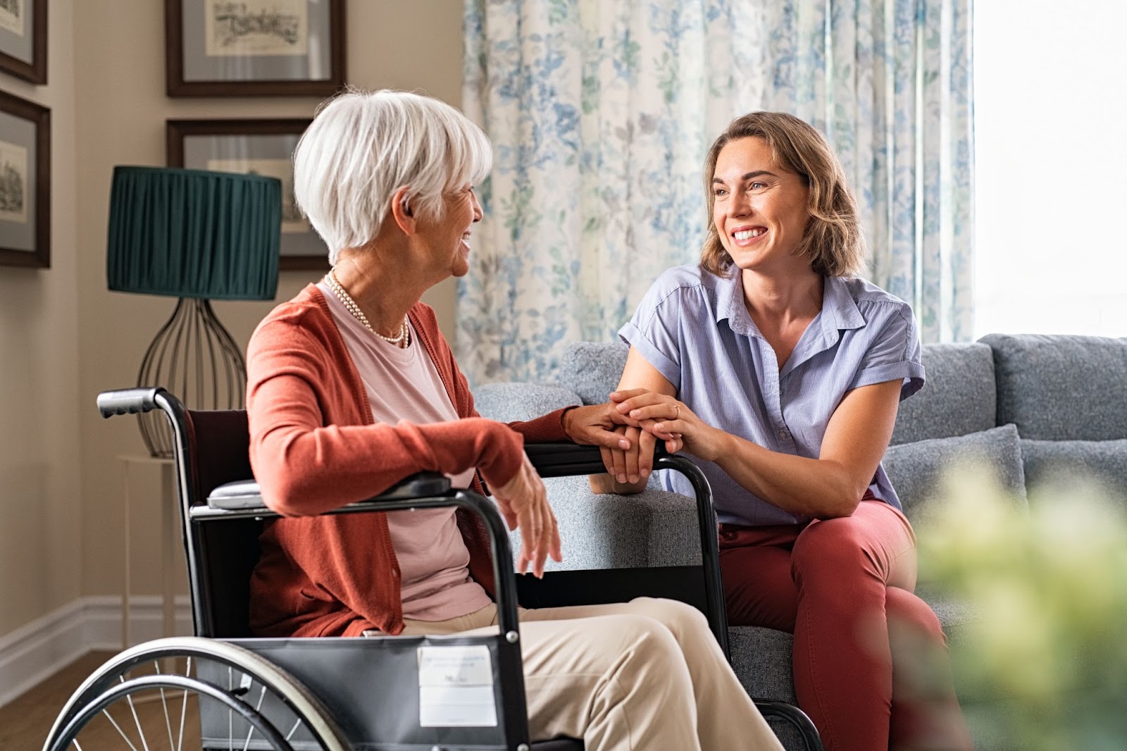 daughter and senior mom in wheel chair smiling in living room