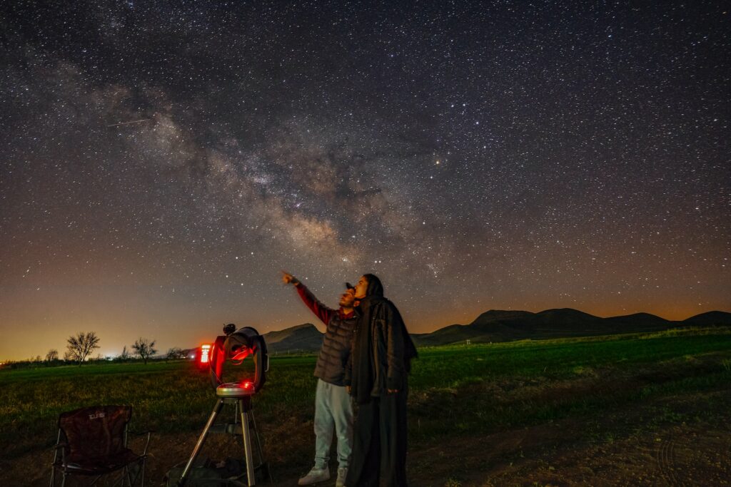 a man standing next to a telescope looking at the stars