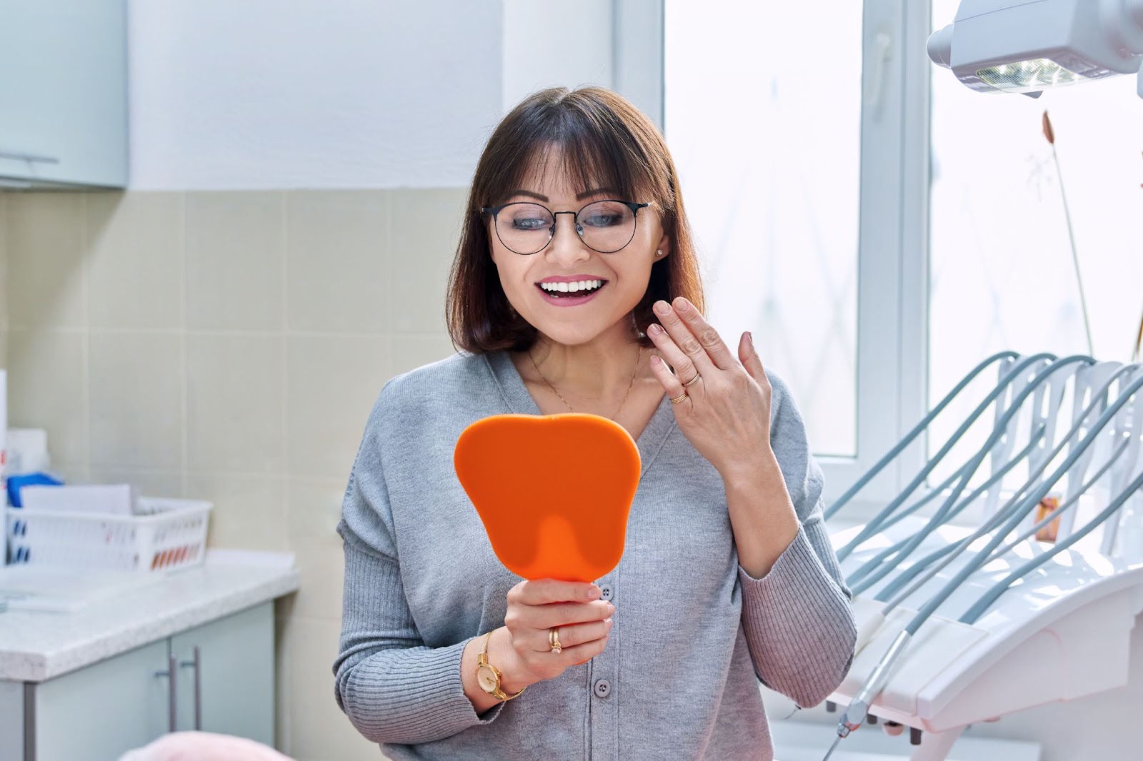 patient with glasses holding a mirror looking at her reflection smiling for her new dental implants