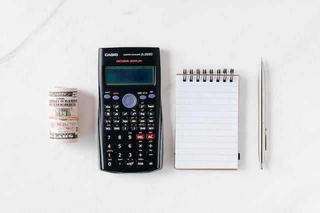 A calculator, a notepad, a pen, and money