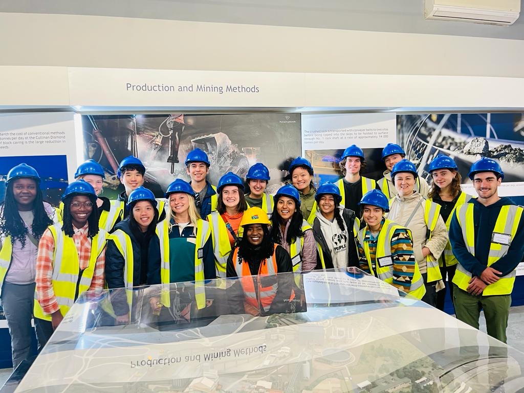 16 students dressed in blue safety hats and yellow safety vests pose for a photo.