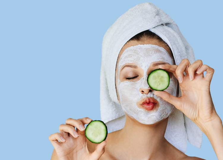 A person with a white mask holding a cucumber slice over her eyes

Description automatically generated