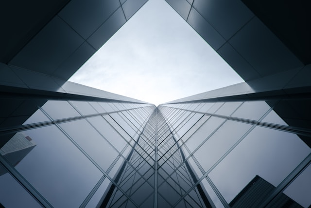 A grey glass building with reflections with a camera angle from below looking up at a clear blue sky