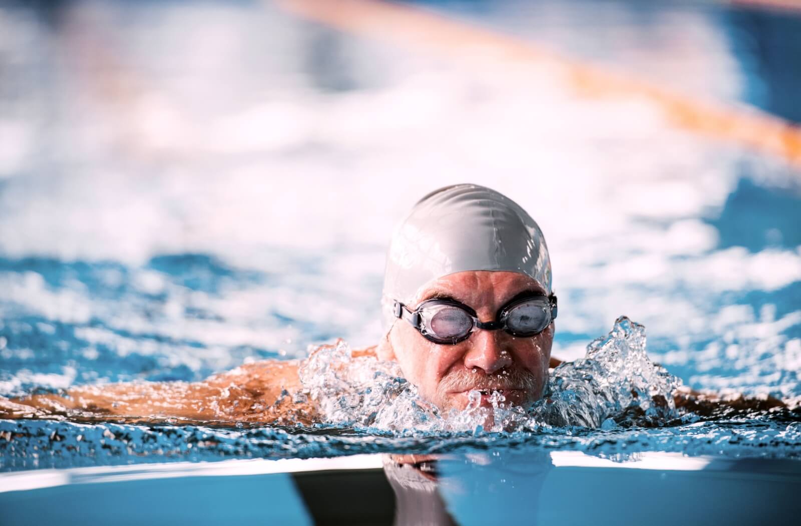 A senior in swim goggles and a cap swimming in a pool to build his strength and endurance.