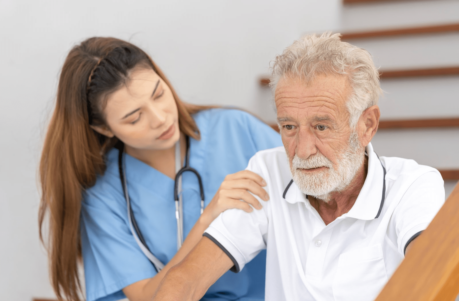 A female nurse helping a senior man walk down the stairs.