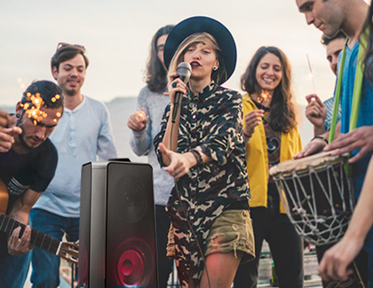 Woman singing with a microphone connected to a Samsung Sound Tower, surrounded by a group of people