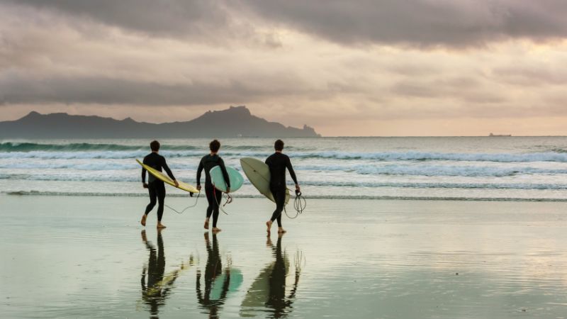 A photo of three surfers walking on a beach.