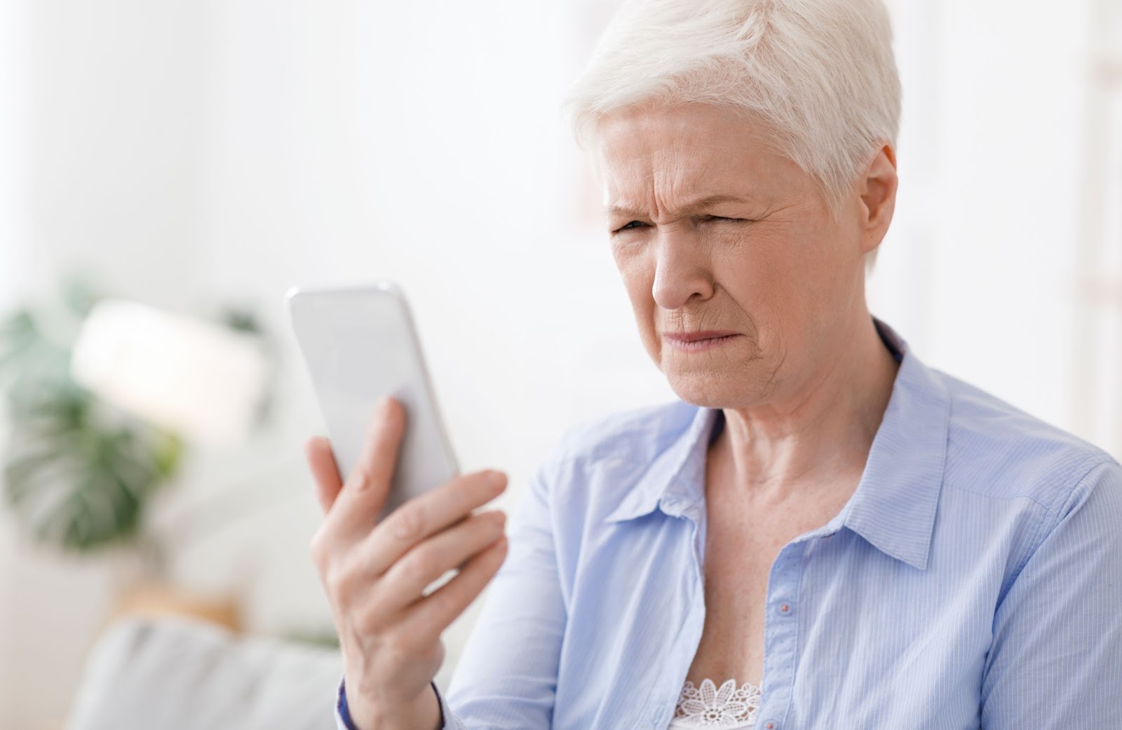 An elderly women squints her eyes as she struggles to see something on her phone.
