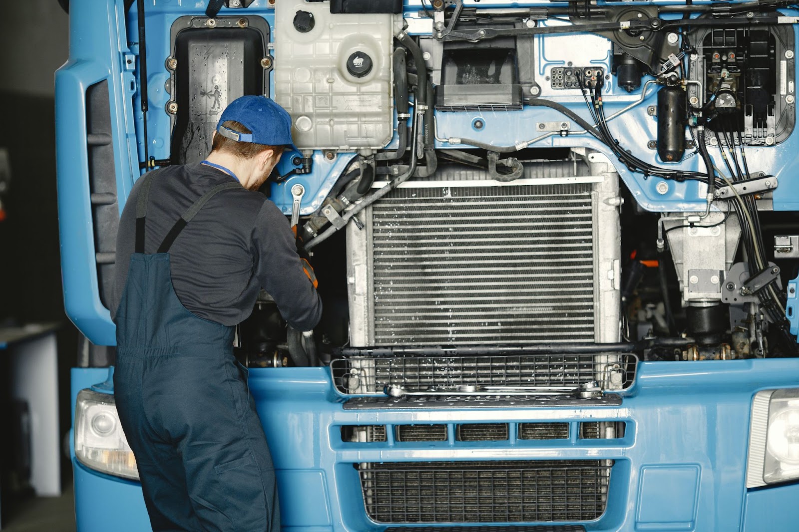 A repair mechanic working under the exposed engine of a semi-truck