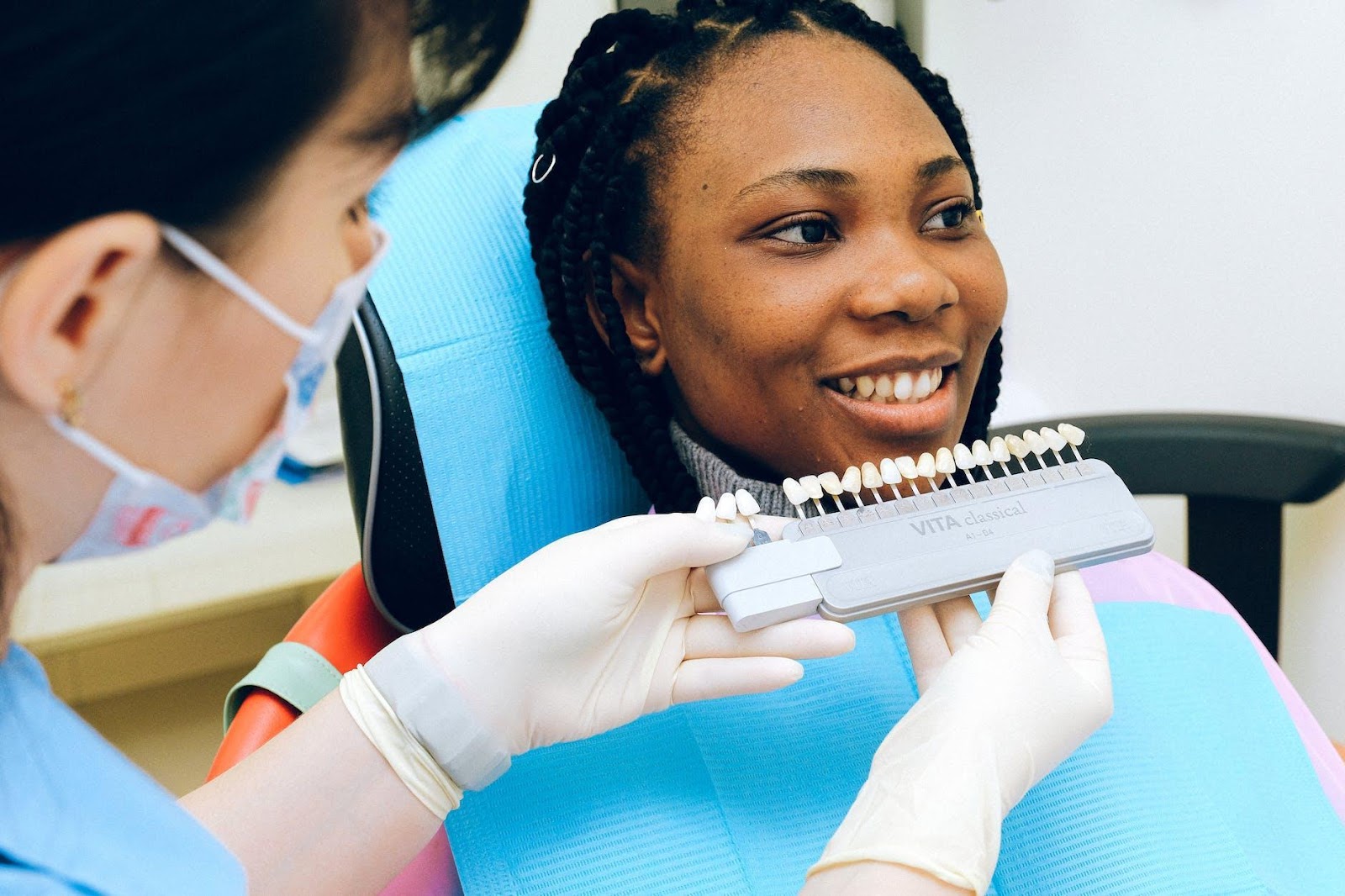 Cheerful black woman sitting in dental chair of modern dentist office and checking teeth implant