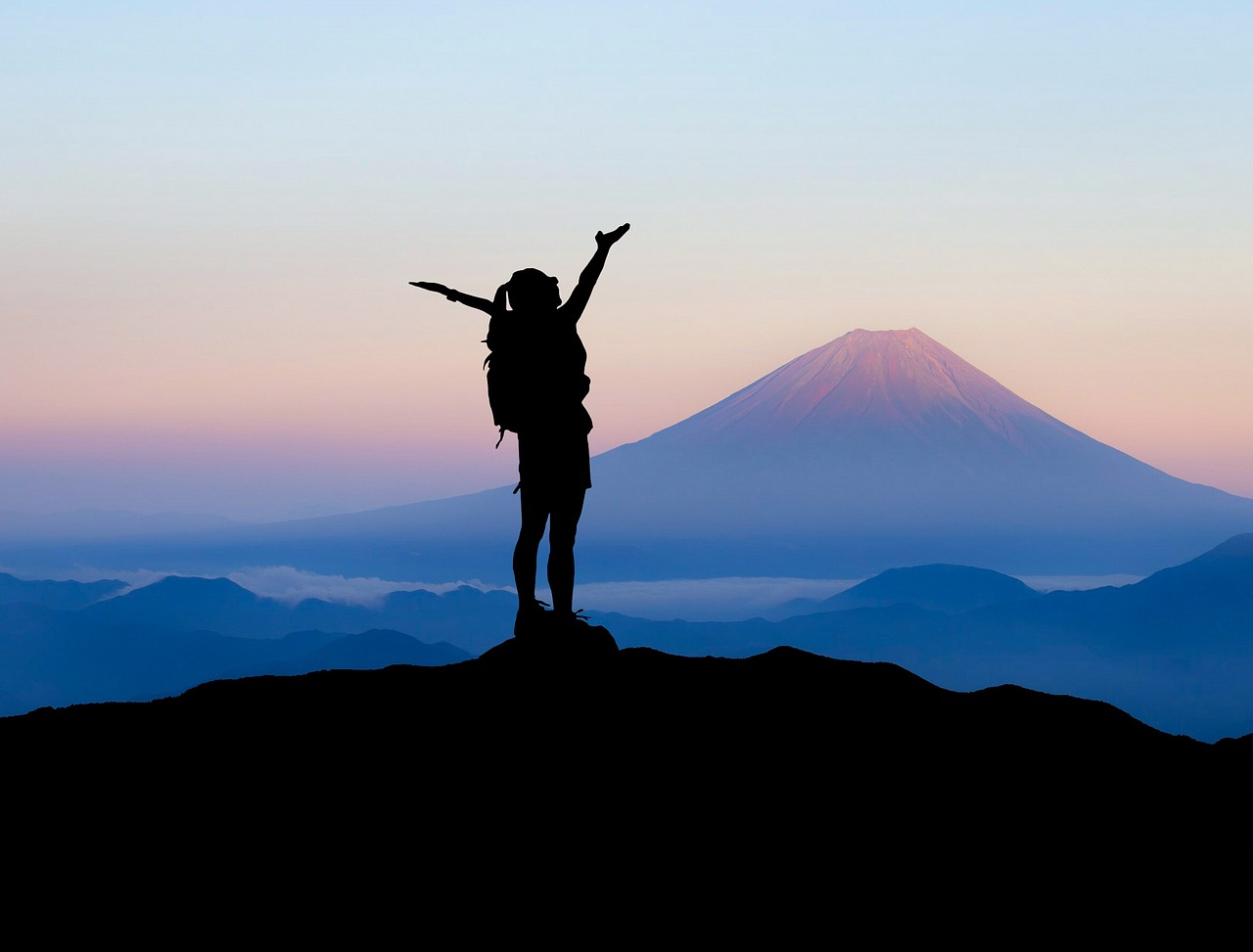 Person standing on top of a hill, a mountain in the background, after successfully facing the challenge of climbing up