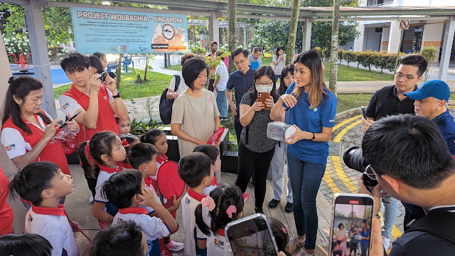 Verily's Program Manager Yanni Yoong explaining to Senior Minister of State for National Development and Foreign Affairs Sim Ann and pre-school children how male male Wolbachia-Aedes mosquitoes are released via hand containers at the expansion of Project Wolbachia in Clementi residential estate.