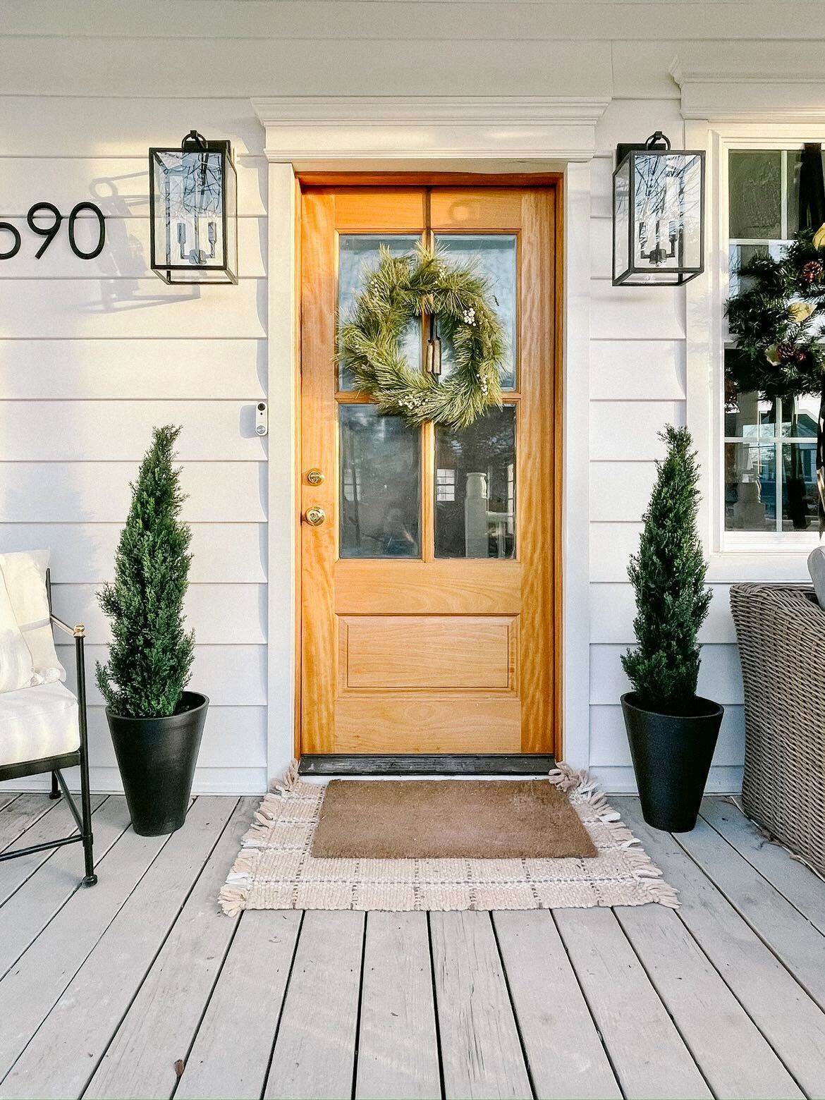 A warm front porch with a wooden door, green wreath, and plants accenting the entryway.