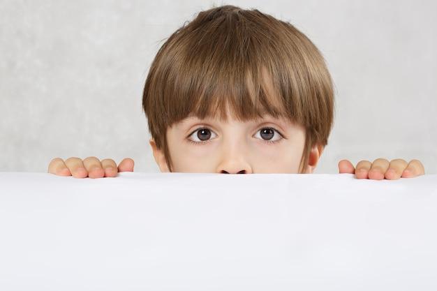 Foto niño de seis años esconde su rostro detrás de la mesa primer plano texto libre