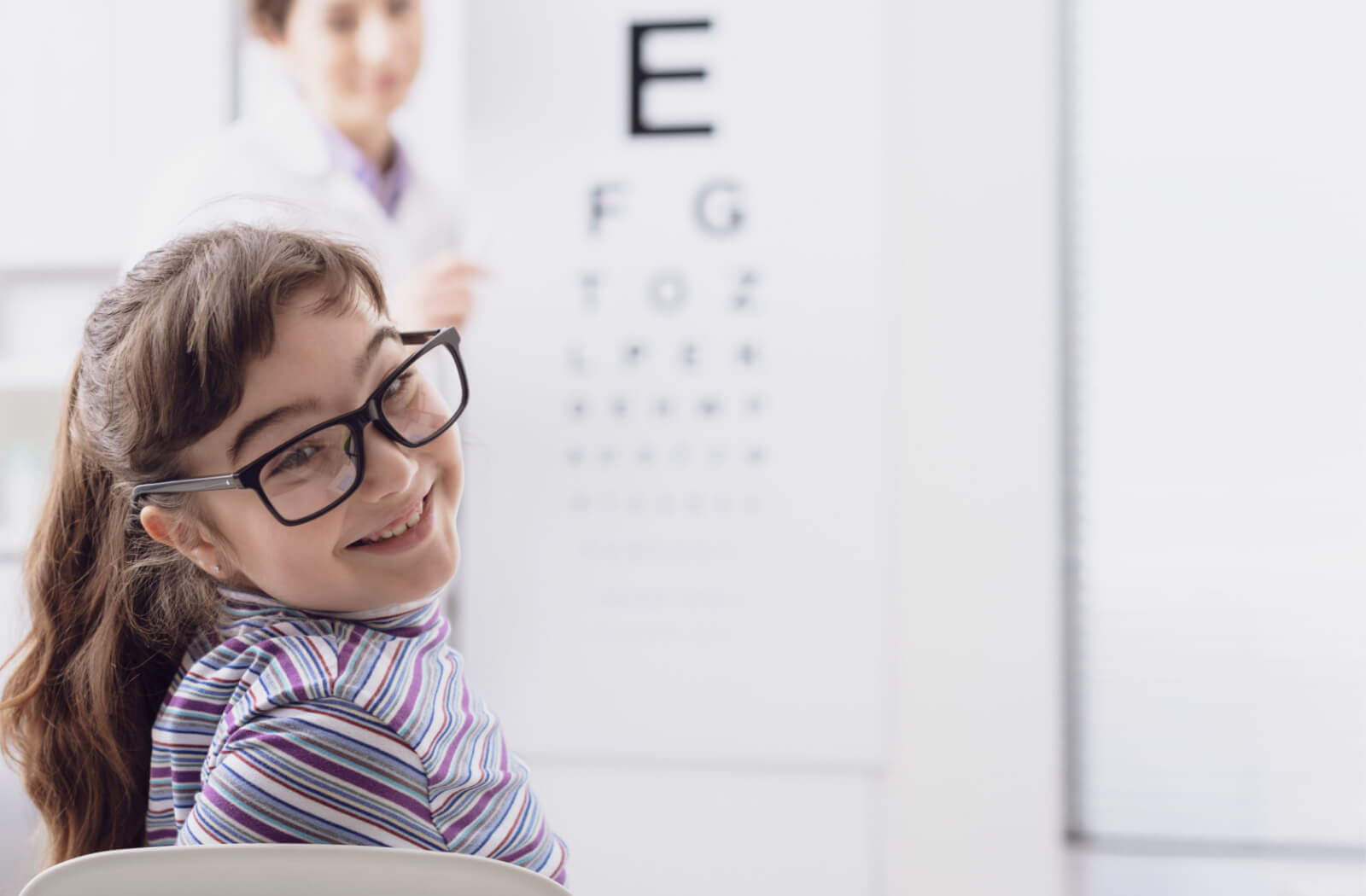 An optometrist conducting an eye exam on a female child with glasses