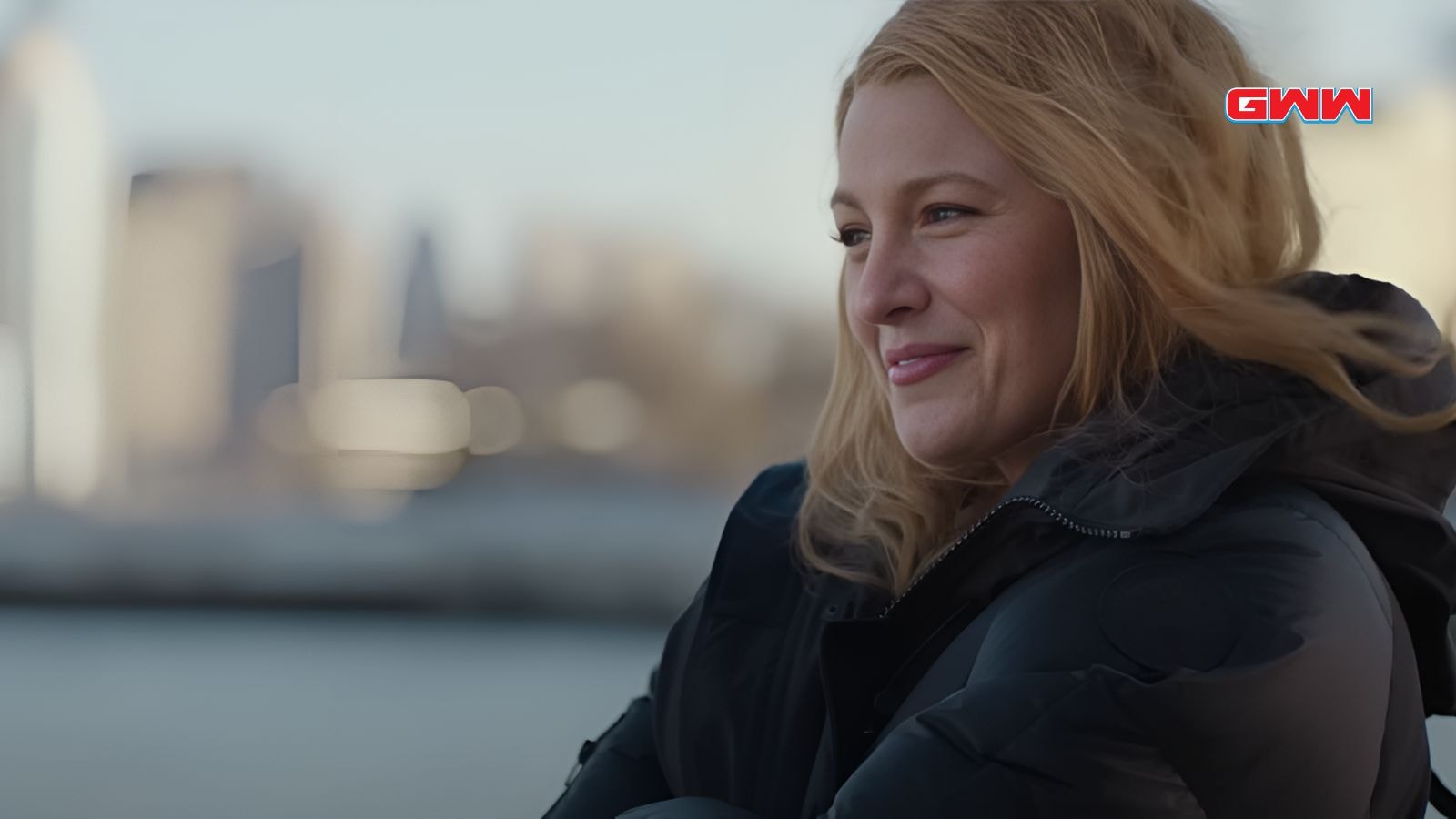 Lily with blonde hair smiling outdoors, wearing a black jacket.