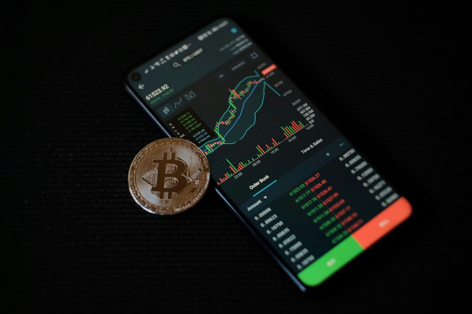 A smartphone displaying cryptocurrency market data next to a Bitcoin coin