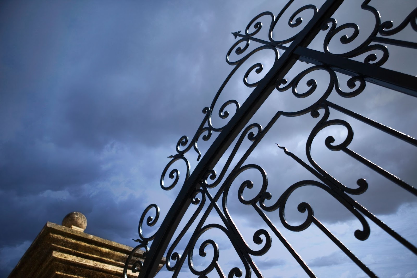 A cropped image of a pair of black gates with dark clouds.