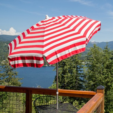 A red and white striped patio umbrella on a table overlooking a lake.