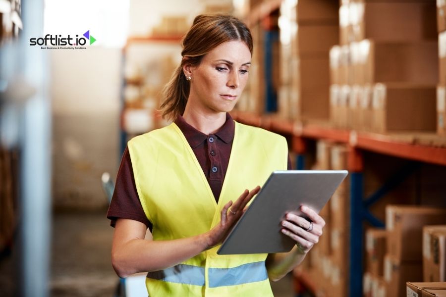 Woman in safety vest using tablet in a warehouse.