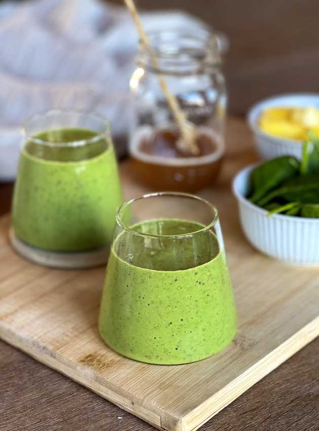 Green kombucha smoothie in a clear glass on a blue textile, with a lime slice.