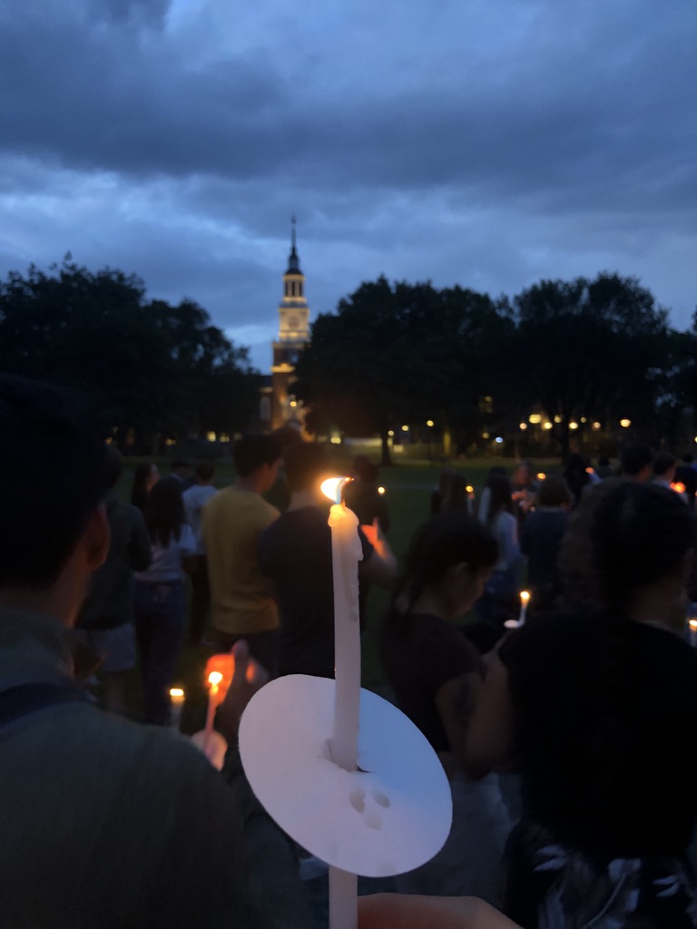 An evening, first-person view of a handheld candle with Baker Berry Library in the background