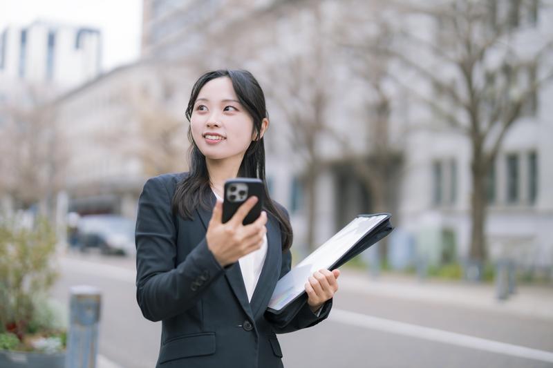 スマートフォンとバインダーを手に持つ女性