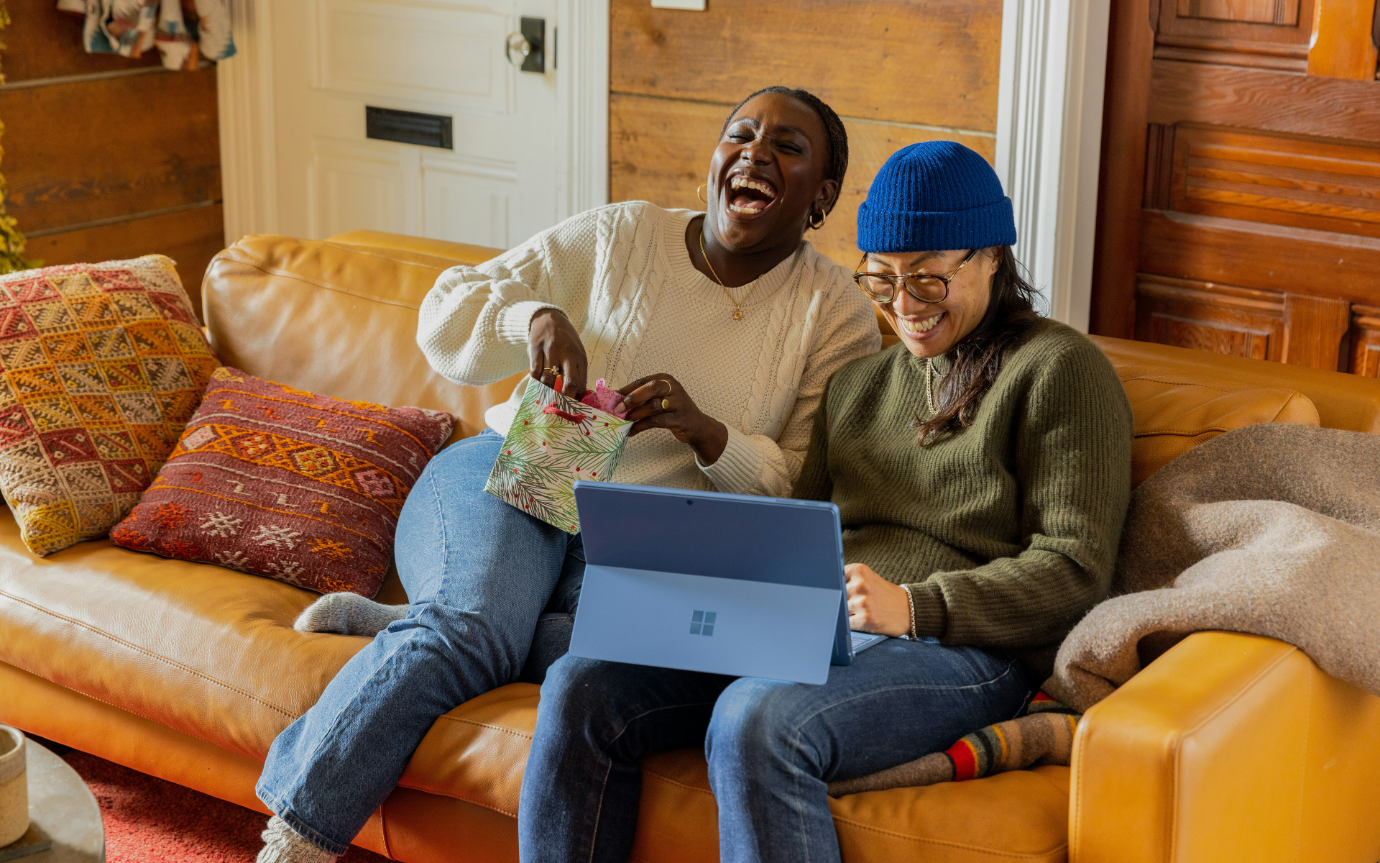 Two women sitting on a couch looking at a computerDescription automatically generated