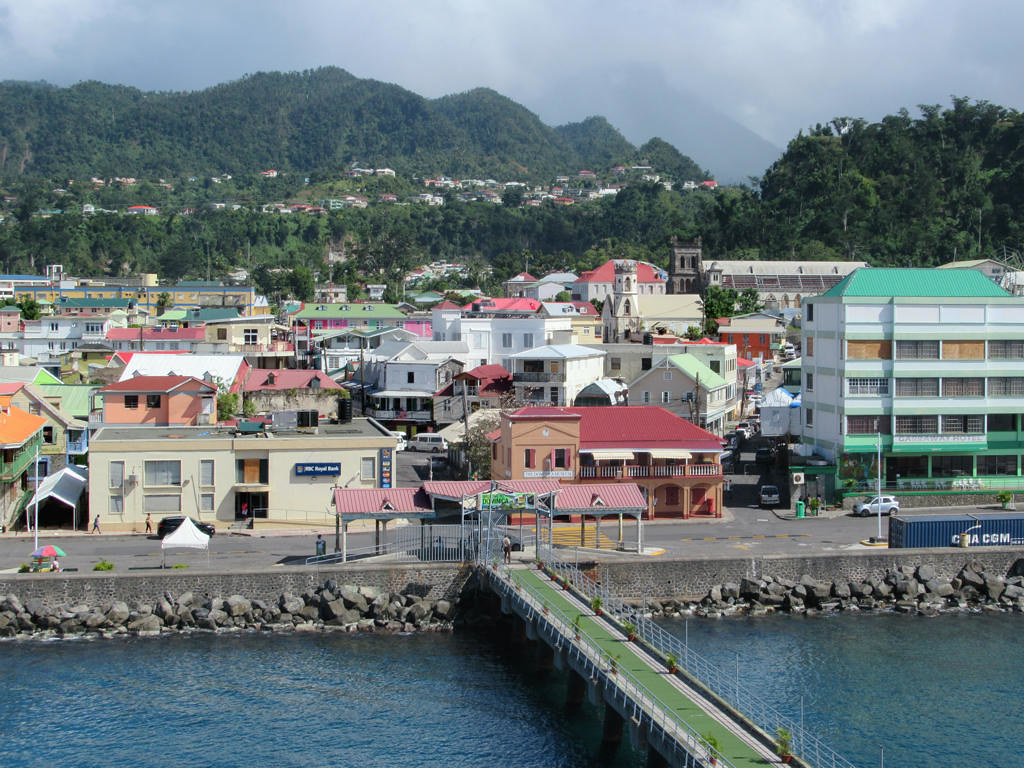 Bridge over a lake in Dominica, with houses at the edge and mountains in the background.