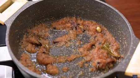 A pan with mustard oil and whole spices such as bay leaves, cumin seeds, and cardamom frying to create a fragrant masala base.