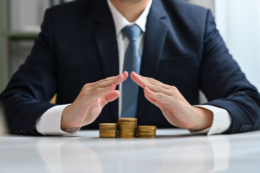 Businessman protecting stacks of coins on a white table.