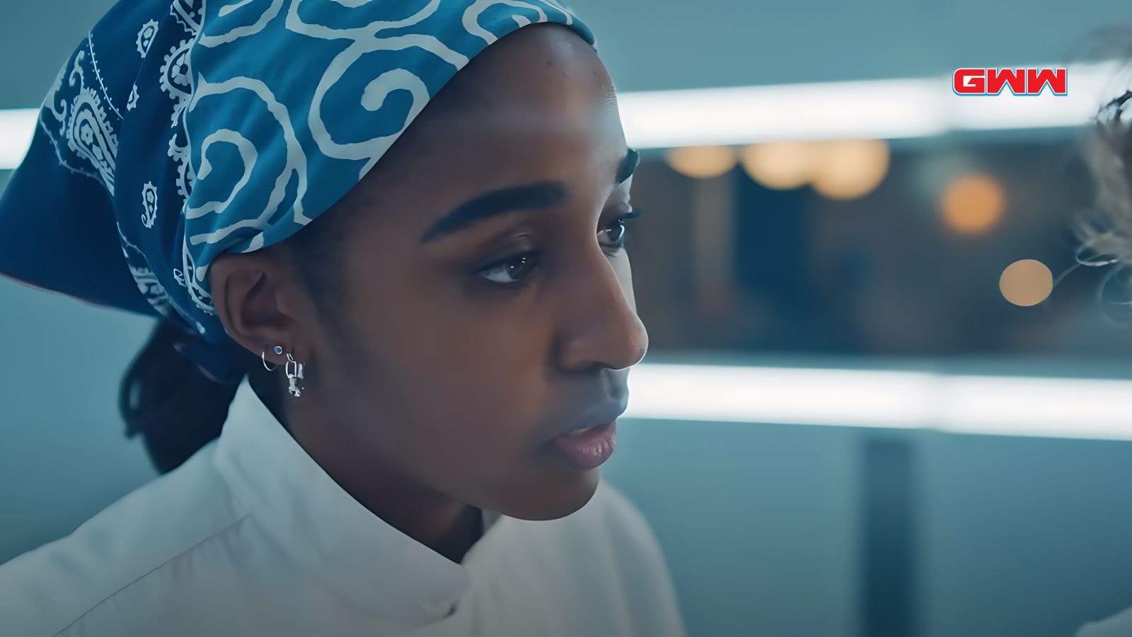 Sydney in a blue bandana looks thoughtfully at someone.