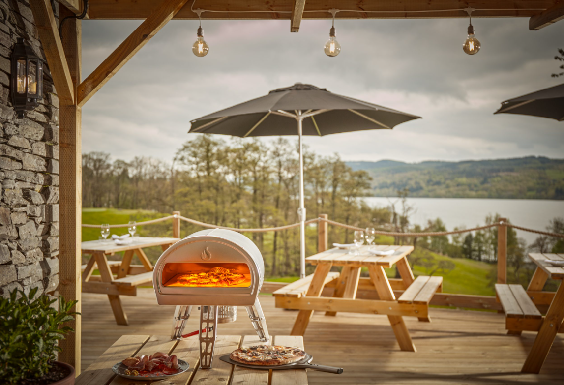 A picnic table with a pizza oven and a lake in the background

Description automatically generated