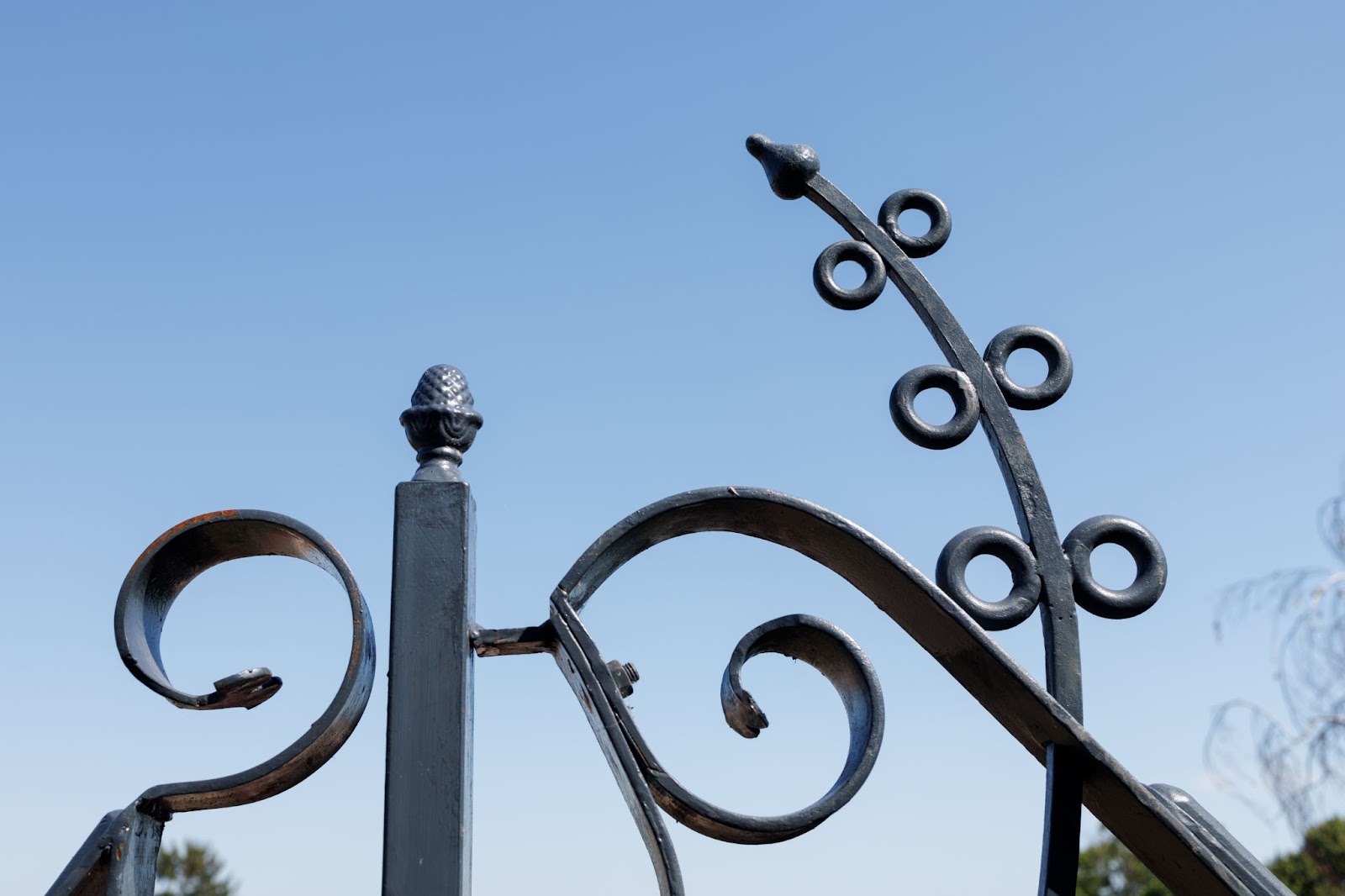 A close-up view of a black steel fence with intricate wrought iron patterns set against a clear sky background.