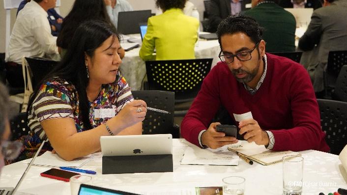 A person and person sitting at a table looking at a cellphone

Description automatically generated