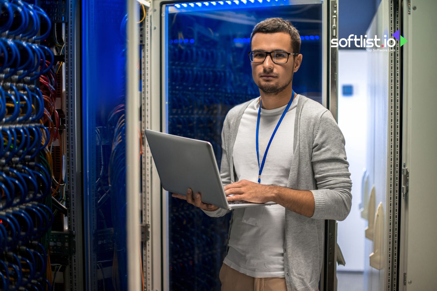 Technician holding a laptop, standing in a blue-lit server room