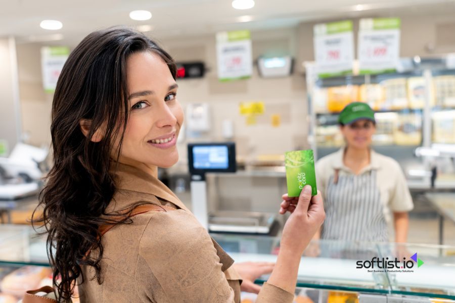 Woman holding a green loyalty card in a supermarket, smiling at the camera.