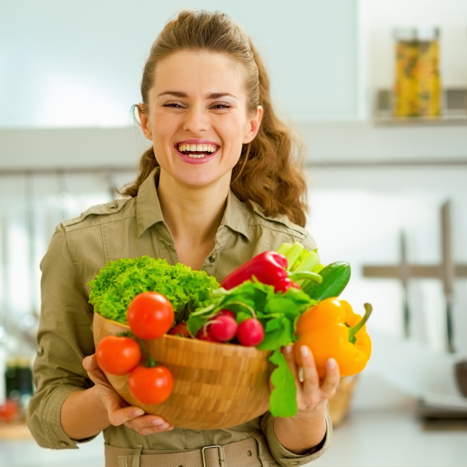 A young woman smiles at the camera while holding a basket full of fresh produce