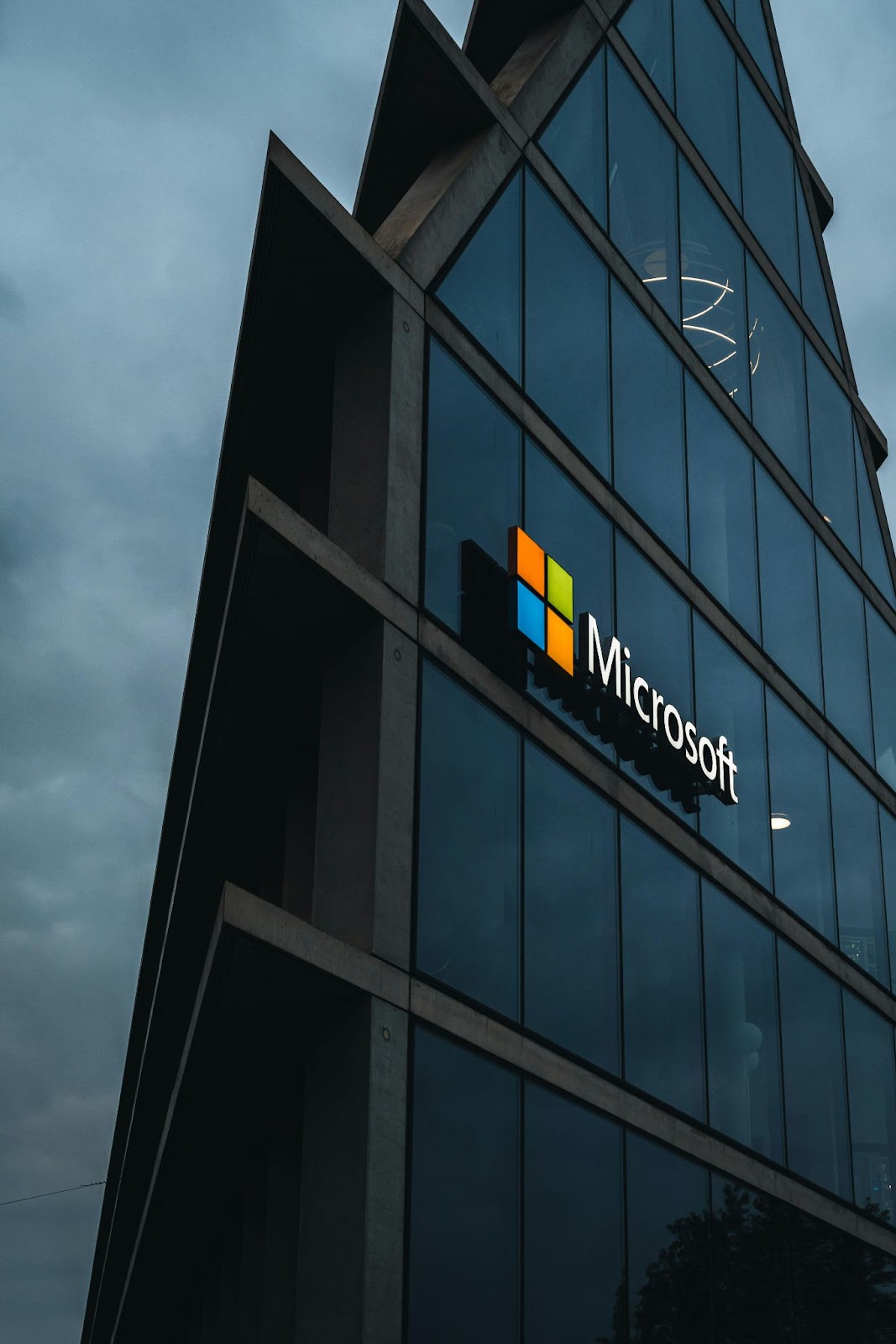 A modern glass building with a prominent Microsoft logo, viewed from a low angle.