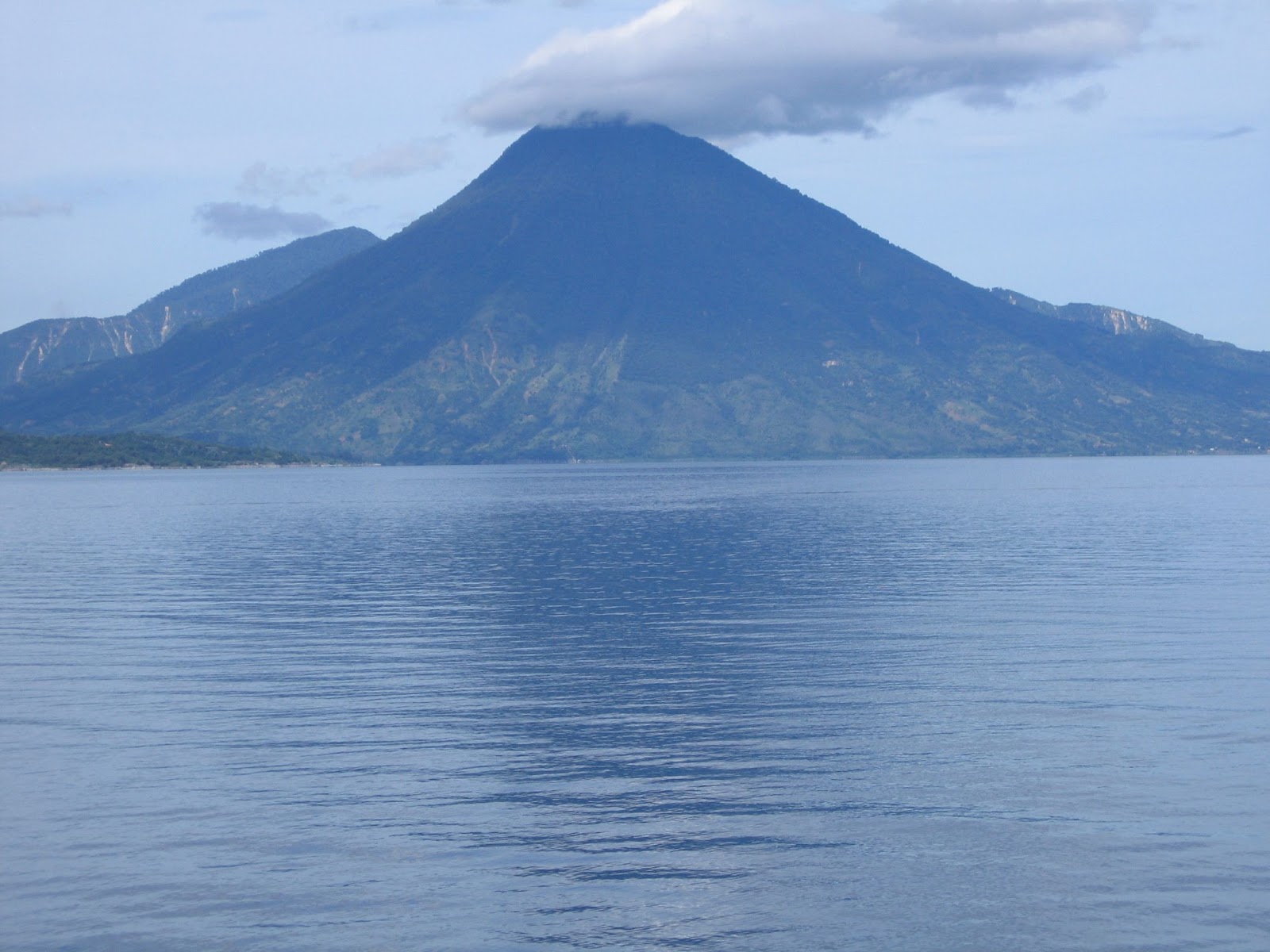 A calm lake with clouds floating on top of Volcán Tolimán against the backdrop of Volcán Atitlán in Guatemala.